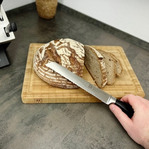Das Brotmesser aus dem Zwilling-35145-007-0-Set liegt auf einem Brotlaib. Bereits geschnittene Scheiben sind zu sehen.