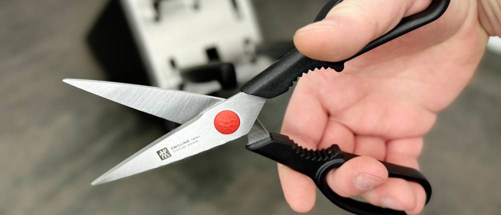 Die Küchenschere des Zwilling-Sets wird in der Hand gezeigt. Der Messerblock ist leicht im Hintergrund zu erkennen.