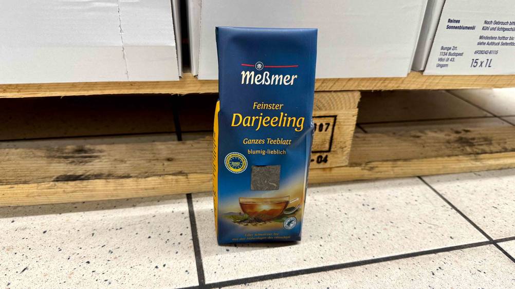Der getestete Meßmer-Tee steht vor einer Holzpalette mit Kartons auf dem Boden.