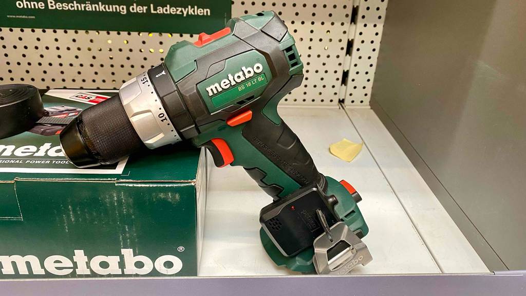 Ein grün-schwarzer Metabo Akku-Bohrschrauber im Test lehnt ohne Akku an seiner Originalverpackung auf einem Ausstellungsregal.