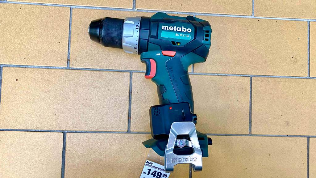 Ein grün-schwarzer Metabo Akku-Bohrschrauber im Test liegt auf der Seite ohne Akku auf beigefarbenen Fliesen inklusive Preisschild in einem Verkaufsbereich.