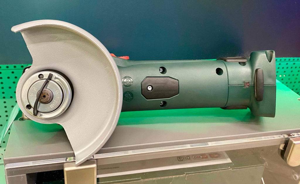 Winkelschleifer-Test: Nahaufnahme auf einen grün-schwarzen Winkelschleifer ohne Akku der Marke Metabo, mit Fokus auf die Schutzhaube aus silberfarbenem Metall.