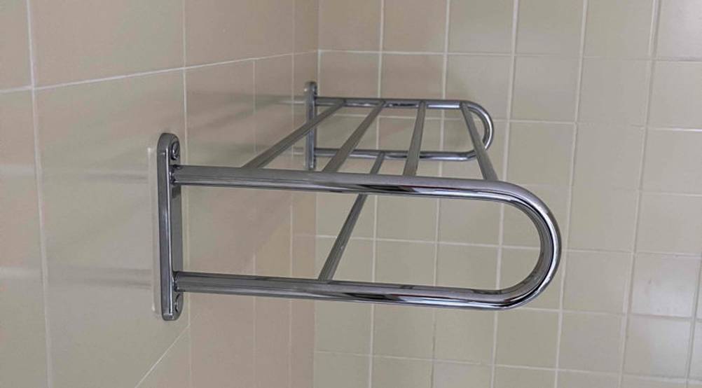 Seitenansicht eines metallfarbenen Wand-Handtuchhalters im Test mit Längsverstrebungen und abgerundeten Seitenhaltern auf beigefarbener Fliesenwand.