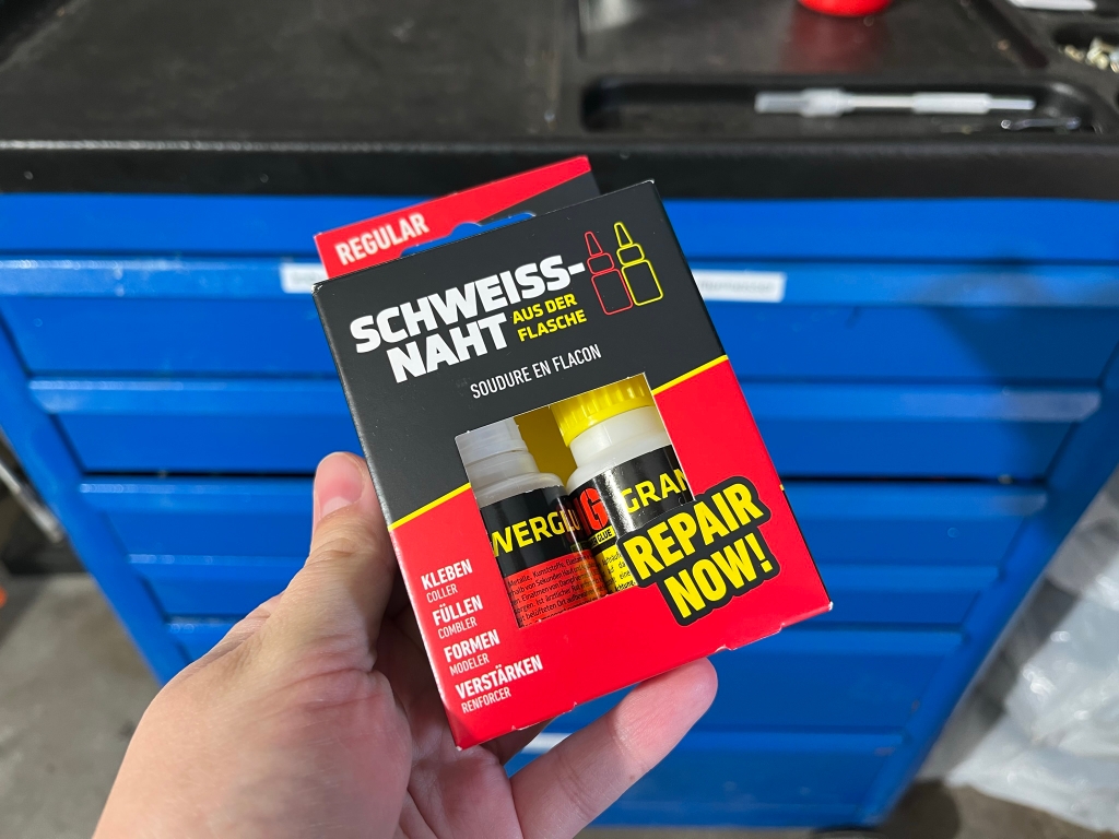 Metallkleber in der Hand vor einem Werkzeugkasten