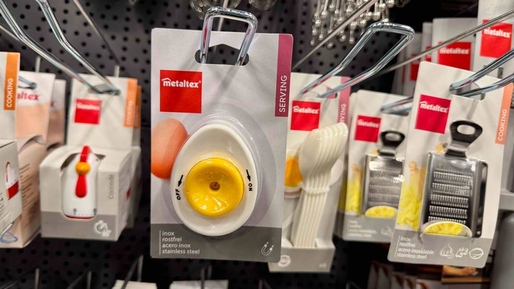 Die Verpackung mit dem getesteten Eierpiekser in Weiß-Gelb hängt an einem Verkaufsregal mit weiteren Küchenhelfern.