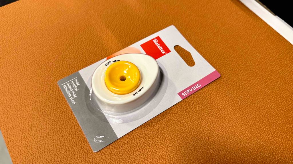 Der getestete Eierpiekser in Weiß-Gelb befindet sich in seiner Verpackung auf einem gelben Hocker.