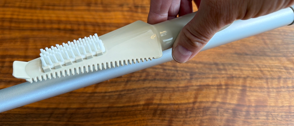 Eine Hand entfernt eine Reinigungsbürste vom Mexerris-Sprühwischer.