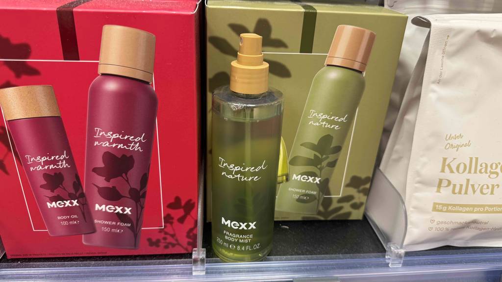 Eine Sprühflasche Körperspray im Test steht vor seiner hellgrünen Verpackung auf einem Regal mit weiteren Körperpflegeprodukten der Marke Mexx.