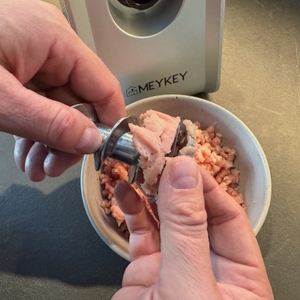 Eine Hand löst Fleischreste vom Zerkleinerer des Meykey-Fleischwolf