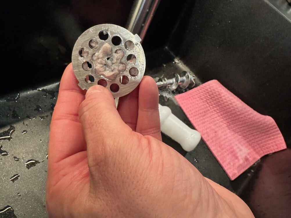 Eine Hand hält den verschmutzten Einsatz des Meykey-Fleischwolf fest