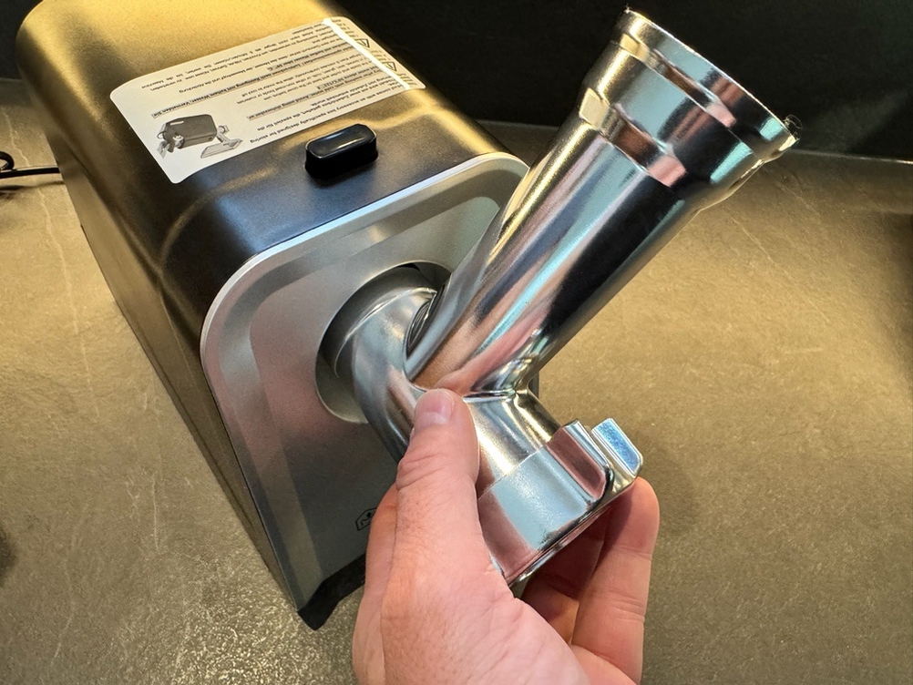 Eine Hand löst die gesamte vordere Einheit durch die das Fleisch zerkleinert wird