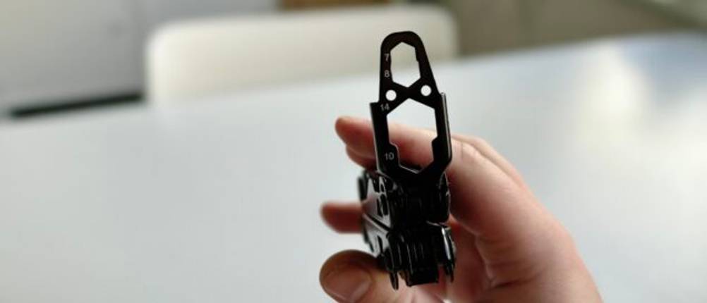Eine Hand hält das Miaoke 23-in-1 Multitool, bei dem der Mehrfachschlüssel sichtbar ist. Der Hintergrund zeigt einen weißen Tisch mit heller Einrichtung.