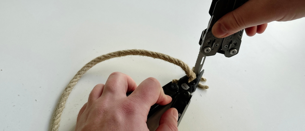 Zwei Hände nutzen das Miaoke 23-in-1 Multitool, um ein Hanfseil mit der Zange zu durchtrennen. Die Zange hat das Seil blockiert und ließ sich nicht mehr öffnen.