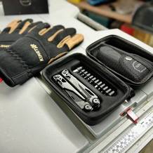 Das Miaoke 23-in-1 Multitool liegt geöffnet in einem schwarzen Aufbewahrungsetui mit mehreren Bits. Daneben befinden sich schwarze Arbeitshandschuhe auf der Werkbank.