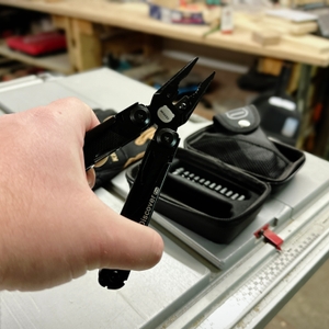 Das Miaoke 23-in-1 Multitool wird geöffnet in einer Hand gehalten und zeigt die Zange mit feinen Zähnen und integriertem Drahtschneider. Im Hintergrund liegt das schwarze Etui mit zusätzlichen Bits.