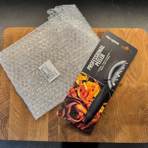 Die Originalverpackung des Sparschälers liegt auf einem Holzbrett.