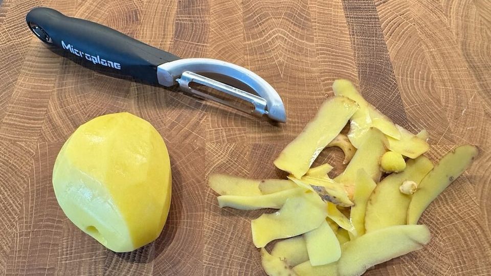 Ein Sparschäler liegt neben einer geschälten Kartoffel sowie deren Schalenstreifen.