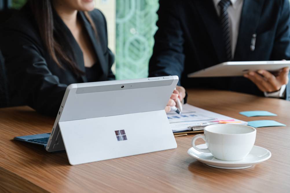 Windows-10-Tablets im Test: Eine Frau arbeitet an einem Microsoft Surface. Neben ihr sitzt ein Mann mit einem Tablet in der Hand. Vor ihr auf dem Tisch steht eine Kaffeetasse.