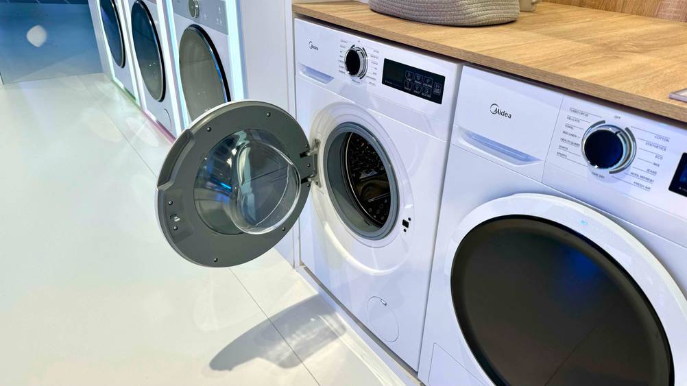 Getestet: Eine Midea-Waschmaschine mit geöffneter Klappe neben anderen Geräten in einer Ausstellung.