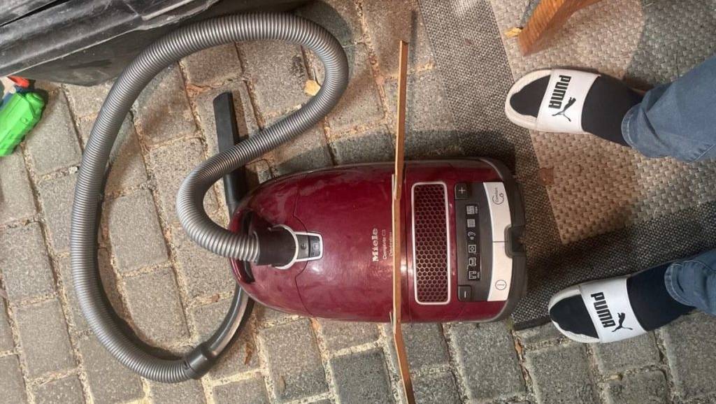 Füße in weißen Puma-Badelatschen neben einem weinroten Miele-Tierhaarstaubsauger im Test auf grauem Pflasterklinker.