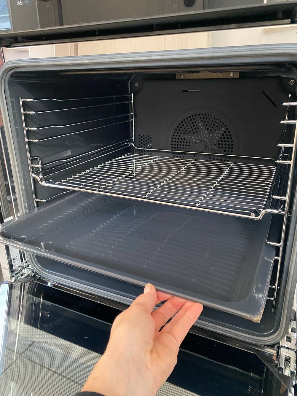 Induktionsherd im Test: Eine Hand zieht die Backbleche aus dem geöffneten Backofen.
