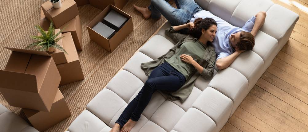 Mietkautionskontos im Test: Ein junges Paar liegt auf einer weißen Couch, während neben ihnen Umzugskartons stehen.