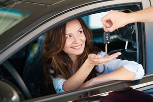 Mietwagenportale im Test: Eine junge Frau sitzt in einem Auto, während eine andere Person ihr durch das Fenster die Autoschlüssel reicht.