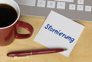 Mietwagenportale im Test: Neben einem Laptop befindet sich eine Kaffeetasse und ein Zettel mit der Aufschrift Stornierung.