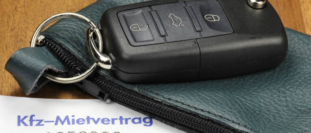 Mietwagenportale im Test: Neben einem Kfz-Mietvertrag liegt ein Autoschlüssel, der an einem kleinen Lederbeutel befestigt ist.