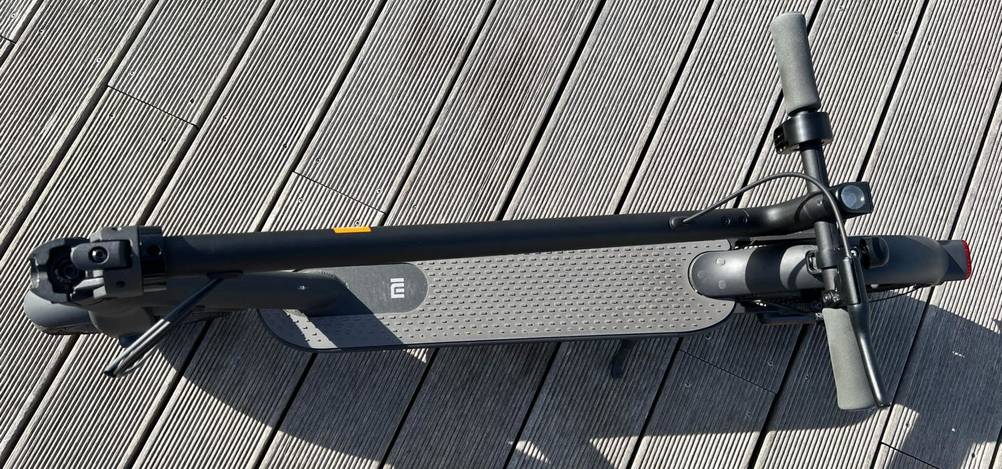 Elektroroller im Test: Ansicht von oben eines dunkelgrauen Modells der Marke Mi, der sich mit eingeklapptem Lenker auf einem grauen Bootssteg befindet.