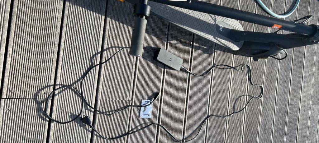 Elektroroller-Test: Ansicht von oben auf ein eingeklapptes Modell neben seinem Ladekabel auf einem Bootssteg.