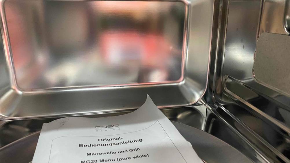 Innenraum einer getesteten Mikrowelle mit Grill und Heißluft, Bedienungsanleitung auf dem Boden.