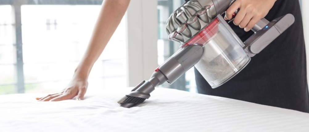 Person reinigt eine Matratze mit einem Milbensauger im Test und stützt sich mit einer Hand auf