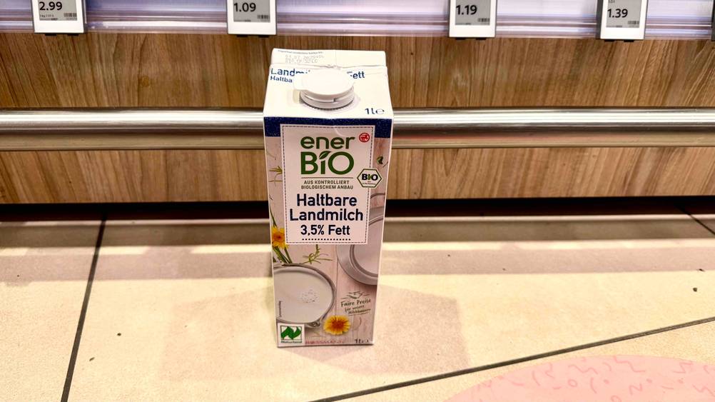 Eine Packung der getesteten Milch von schräg oben vor einem Regal mit Preisangaben.