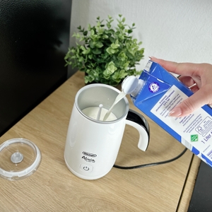 Milch wird aus einem Karton in den offenen De'Longhi EMF 2.W Milchaufschäumer gegossen. Der Deckel liegt daneben auf der Arbeitsfläche.