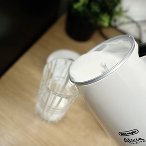 Der De’Longhi EMF 2.W Milchaufschäumer wird über ein Glas gehalten. Milchschaum wird aus dem Behälter vorsichtig ausgegossen.
