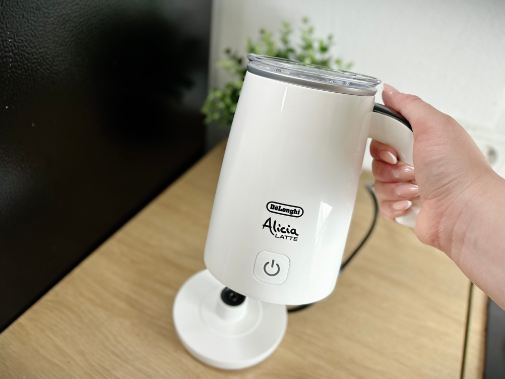 Nahaufnahme des De’Longhi EMF 2.W Milchaufschäumers, gehalten an der Basisstation. Der Griff und das Bedienelement sind gut sichtbar.