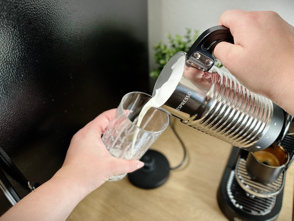 Ein Glas wird mit aufgeschäumter Milch aus dem Nespresso Aeroccino 4 befüllt. Der Milchaufschäumer wird dabei mit einer Hand gehalten.