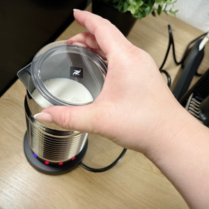 Eine Hand legt den transparenten Deckel auf den Nespresso Aeroccino 4 Milchaufschäumer. Im Gerät befindet sich bereits Milch.