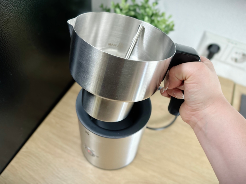 Der Edelstahlbehälter des WMF Lono Milk & Choc wird aus der Basis gehoben. Eine Hand greift den Griff für den sicheren Halt.