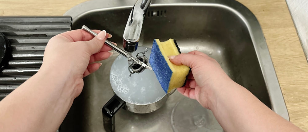 Der Quirl des WMF Lono Milk & Choc wird unter einem Wasserhahn gereinigt. Eine Hand hält einen Schwamm, die andere den Stab.