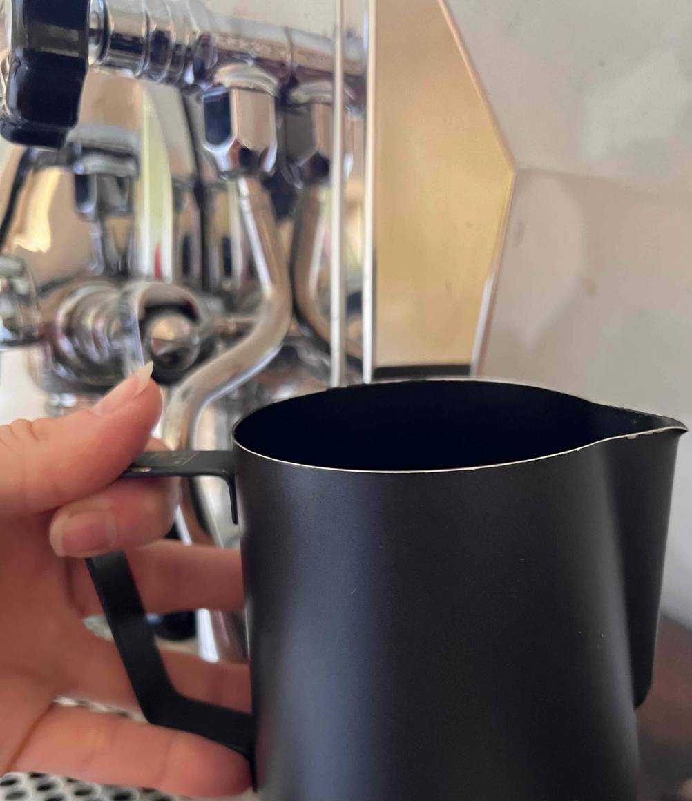 Ein getestetes Milchkännchen befindet sich vor einem Kaffeevollautomaten. 