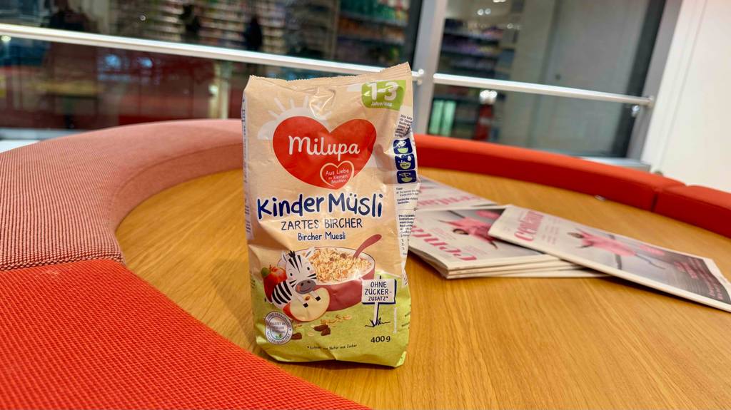 Eine Packung Kindermüsli steht zum Testen auf einer Holzfläche, im Hintergrund sind Zeitschriften.