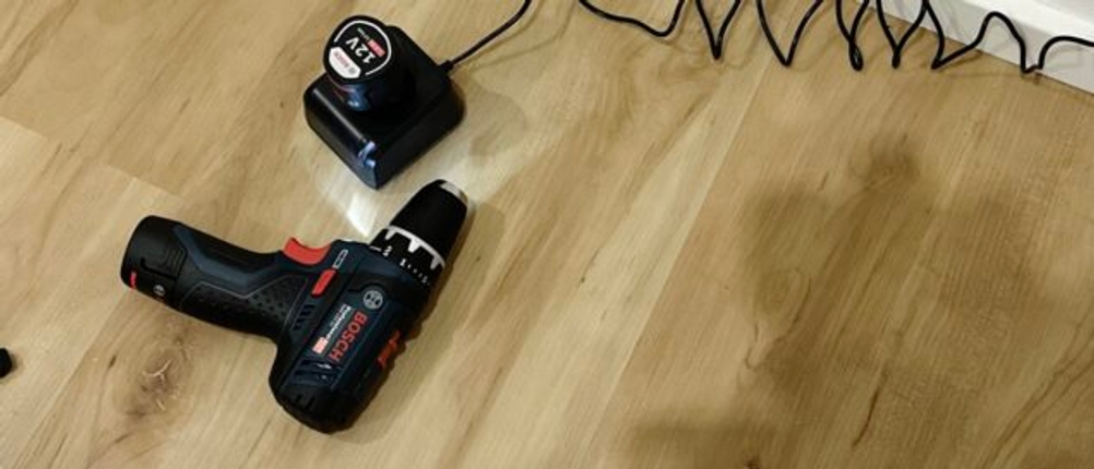 Der Mini-Akkuschrauber von Bosch liegt mit eingeschaltetem Licht neben der Ladestation