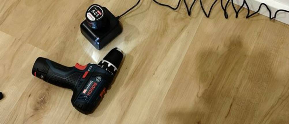 Der Mini-Akkuschrauber von Bosch liegt mit eingeschaltetem Licht neben der Ladestation