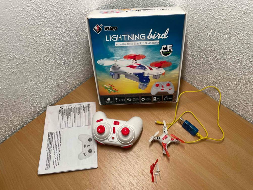 Vor der Originalverpackung liegen der getestete Mini-Quadrocopter, die Bedienungsanleitung, Controller und ein USB-Kabel.