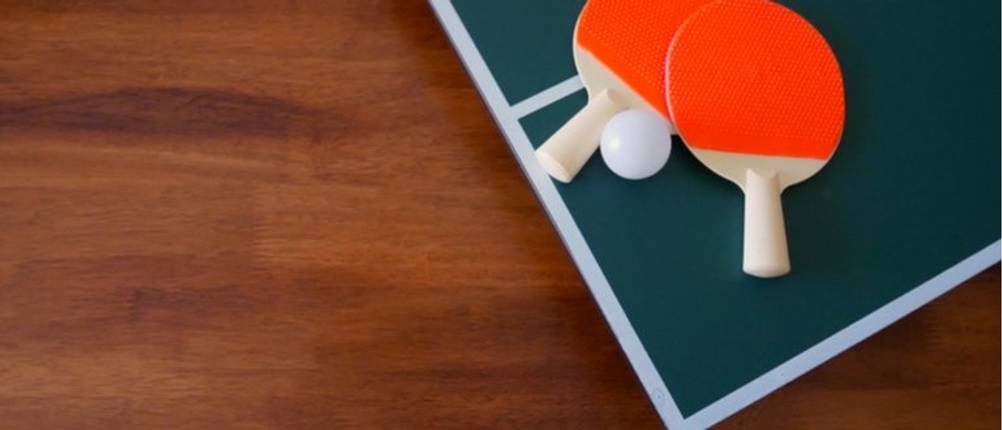zwei Tischtennisschläger und ein Tischtennisball liegen auf einer Tischtennisplatte