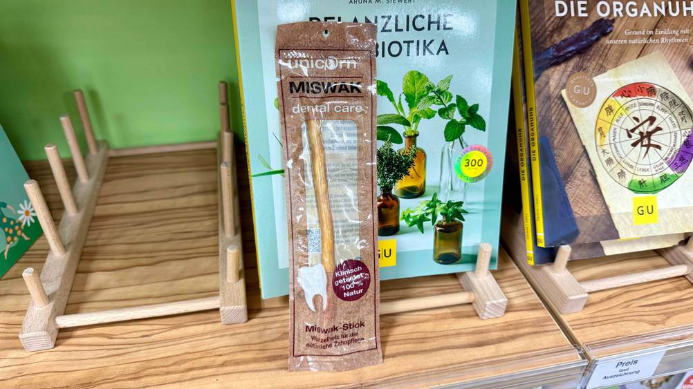 Auf eine Regal vor einem Buch steht eine Packung des Miswak im Test.