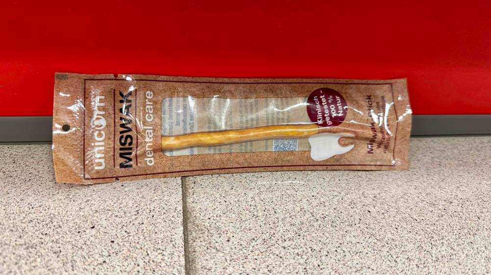 Vor einer roten Wand auf dem Boden liegt eine Packung des getesteten Miswak.