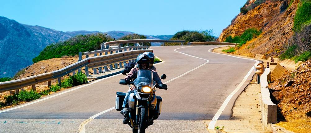 Paar auf Motorrad auf einer Küstenstrecke Sardiniens.